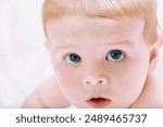 Sweet baby with mesmerizing blue eyes peacefully lying on a cozy bed. Gazing up with a curious and innocent expression. Radiating happiness and health. Embodying childhood