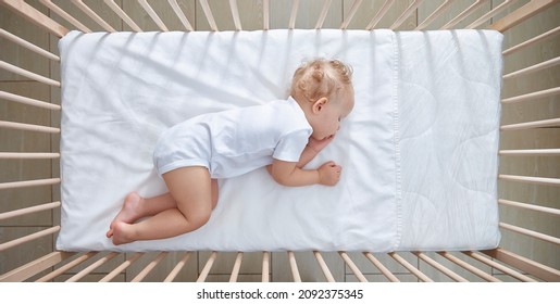Sweet baby sleeps in his crib on a white sheet without drawings. A bright room.