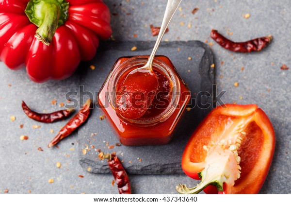 Sweet bell pepper and\
chili pepper sauce, confiture, jam in a glass jar. Grey stone\
background. Top view
