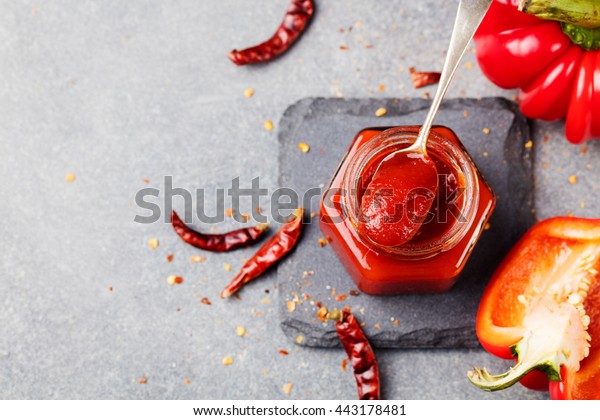 Sweet bell\
pepper and chili pepper sauce, confiture, jam in a glass jar. Grey\
stone background. Top view. Copy\
space