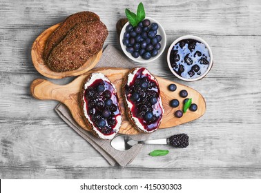 Sweet berry crostini sandwiches with blackberry jam and berries blueberries, whole grain bread for sandwiches, sandwiches board, spoon, mint leaves on a bright white background wooden, top view - Powered by Shutterstock