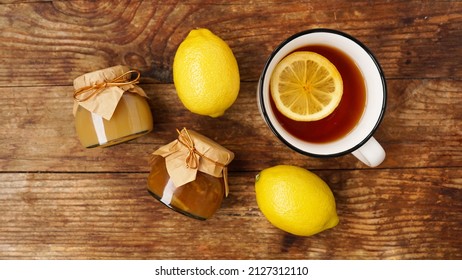 Sweet breakfast. Cup of black tea with lemon. Lemons and jars with homemade jam, marmalade or curd on a wooden table. Top view, flat layout