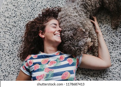 Sweet Brown Spanish Water Dog Playing With Her Owner And Licking Her Face. Enjoying A Great Time Together. Lifestyle At Home, Love