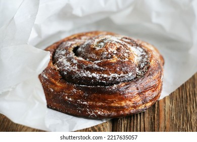 A Sweet Bun With Chocolate Lies In A White Paper Bag On A Wooden Table.