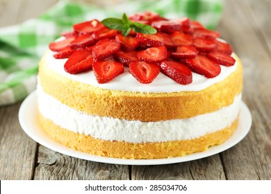 Sweet cake with strawberries on plate on grey wooden background