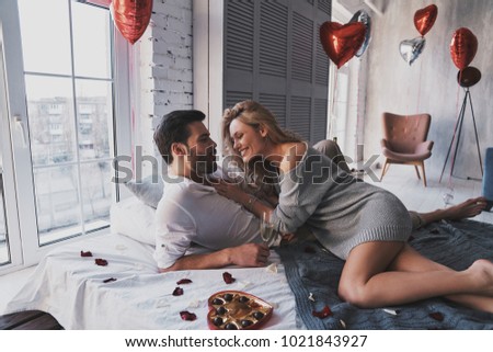Sweet candies in bed.  Beautiful young couple eating chocolate candies and smiling while lying on the bed at home