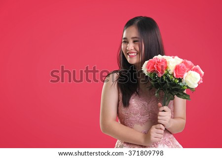 Sweet cheerful Asian teenage girl with natural smile holding a bouquet of roses, looking sideways at copy space on pink background for Valentines Day