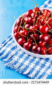 Sweet Cherries On A White Plate. Ripe Cherries And A White-blue Napkin On A Blue Background