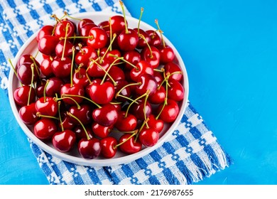 Sweet Cherries On A White Plate. Ripe Cherries And A White-blue Napkin On A Blue Background. Copy Space