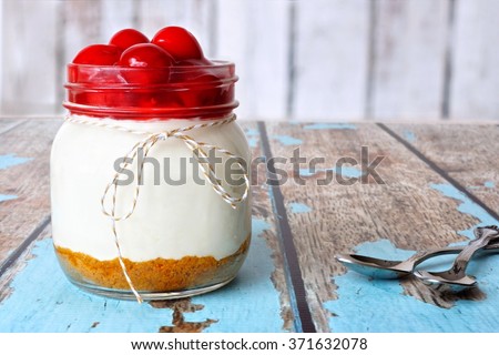 Sweet cherry cheesecake in a mason jar on a rustic wood background