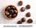 Sweet chestnuts in a wooden bowl on linen. Raw, whole and unshelled Castanea sativa, can be eaten raw, candied, cooked, milled into flour, or in the wintertime roasted as a warm snack on the streets.