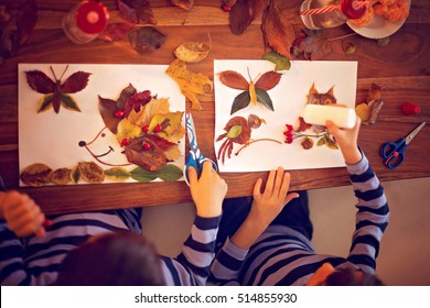 Sweet child, boy, applying leaves using glue while doing arts and crafts in school, autumn time