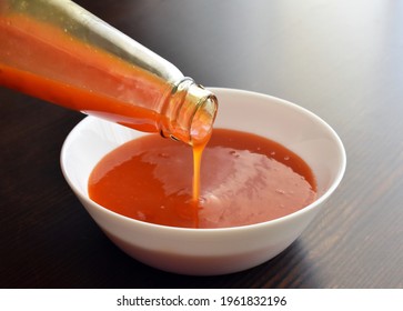 Sweet Chilli Sauce Pouring From A Bottle Into A White Bowl. 