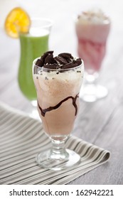 Sweet Chocolate Cocktail With Whipped Cream And Crashed Oreo Cakes Served In Long Glass. Fresh Desserts Composition With Strawberry Shake And Kiwifruit Mousse On The Background.