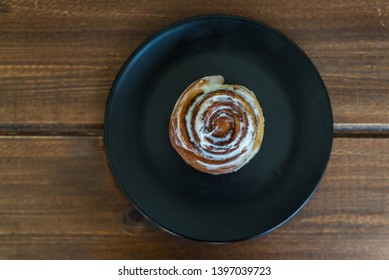 Sweet Cinnamon Bun Roll Swirl Over The Black Plate Top View, Flat Lay 