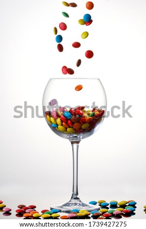 sweet colorful Candy coated chocolate falling in to a glass on white background.