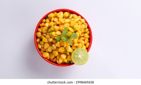 Sweet Corn Chat Or Steamed Yellow Sweet Corn, Chat Masala And Lemon, Served In Red Bowl. Indian Chat Or Snack. Top View Sweetcorn Or Sweet Corn On Isolated White Background