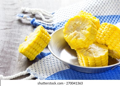 Sweet Corn Cob Pieces On Wooden Table With Navy Blue Kitchen Towel