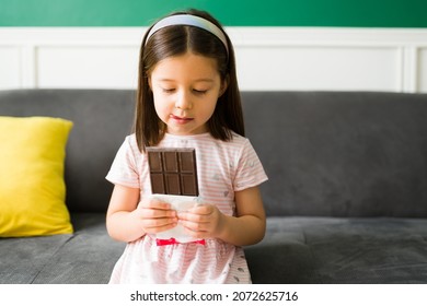 Sweet Cravings. Adorable Elementary Girl Receiving A Treat And Licking Her Lips While Holding A Big Chocolate Candy Bar 