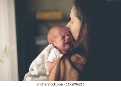 Sweet crying newborn baby at mom on hands, concept real interior, natural lifestyle photo