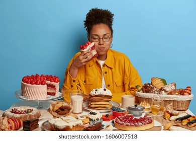 Sweet Delicious Bite. Dark Skinned Curly Woman Wears Round Glasses, Dressed In Yellow Shirt, Has Good Appetite, Eats Desserts, Wears Round Big Glasses And Yellow Shirt. Gluttony And Temptation Concept