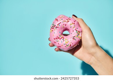 sweet delicious donut with pink frosting on it in hand of unknown female holding it on pink backdrop - Powered by Shutterstock