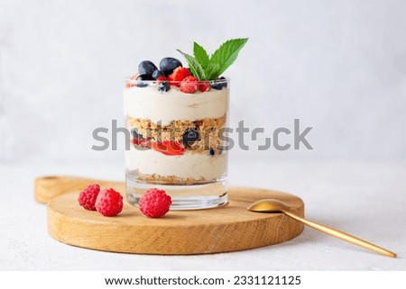 Sweet dessert in a glass with berries, mint, whipped cream and biscuit on a wooden board. Healthy food, vegan, sugar, gluten and lactose free. Berry dessert, cheesecake, trifle, mouse in a glass.