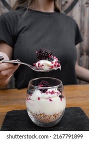 Sweet Desserts. Closeup View Of A Woman's Hand Holding A Spoon And Eating A Glass With A Trifle With Yoghurt, White Chocolate Cream, Cereals And Red Berries. 