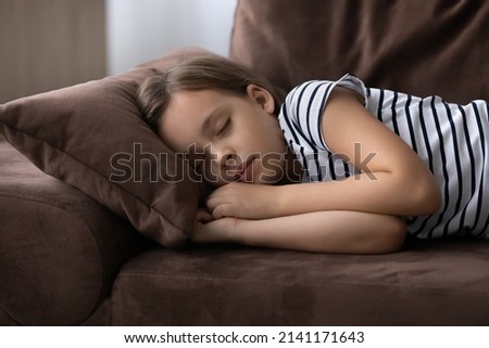 Sweet dreams. Cute little preteen girl sleep dream nap on cozy couch lying in comfortable pose with closed eyes. Tired tween child kid fall asleep on comfy sofa in silent living room after active day