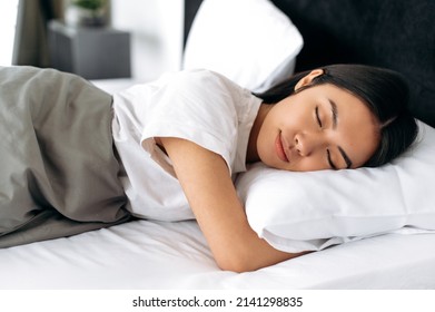 Sweet dreams. Pretty chinese woman in white t-shirt under the blanket in bed in the morning. Side view of a sleeping asian girl in a cozy bed in apartment, pleasant dreams, healthy sleep - Shutterstock ID 2141298835