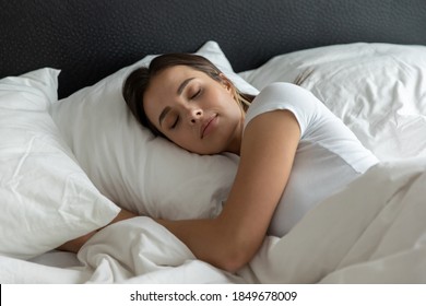 Sweet Dreams. Relaxed Young Female Sleeping In Large Cozy Bed At Home Or In Hotel Suite Room On Clean White Bedclothing Hugging Soft Pillow Covered With Warm Blanket Dreaming Resting Having Pleasure