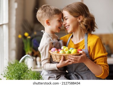 Sweet family portrait of happy mother and little son holding wicker basket full of painted multi-colored Easter eggs, tenderly embracing and smiling in cozy light kitchen at home, selective focus - Shutterstock ID 2127588434