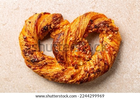 Sweet French soft pretzel or bretzel with puff pastry, almonds and custard cream. A type of baked dessert made from dough that is shaped into a knot. Beige background.