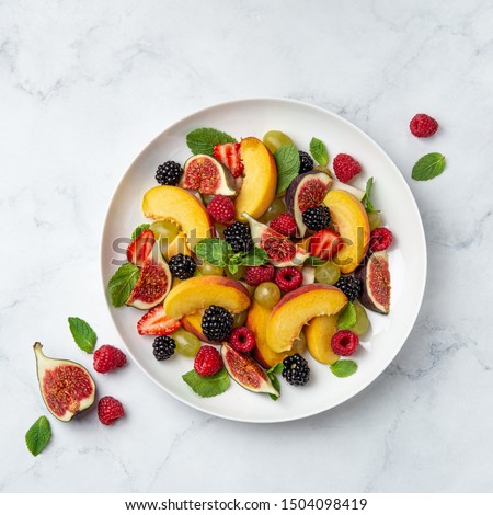 Sweet fruit and berry salad on white plate, marble baground, top view, square image