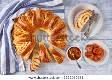 Sweet fruit cake, easter wreath with dried apricot filling, sliced on a pieces on a white wooden background with one piece on a white plate with dessert cutlery, top view, flat lay 