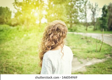 Sweet Girl Outdoors With Curly Hair In The Wind. Back View