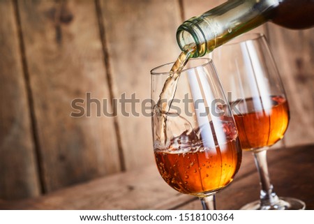 Sweet golden fortified sherry from Andalusia, Spain being served in elegant wineglasses in a close up on the neck of the bottle over wood with copy space angled at a slant with freeze motion splash