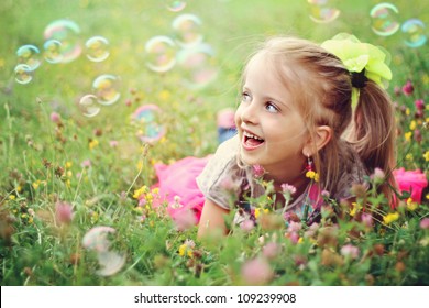 Sweet, happy, smiling six year old girl laying on a grass in a park playing with bubbles and laughing - Powered by Shutterstock