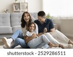 Sweet home. Laughing candid millennial spouses with preteen child mother father little daughter enjoy funny indoor activity messing tickling on floor with heating play in crazy naughty mood on weekend