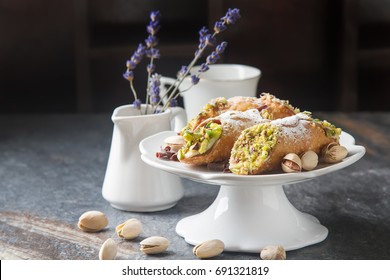 Sweet homemade cannoli stuffed with ricotta cheese cream and pistachios. Traditional Sicilian dessert. Italian pastry. selective focus. Lavender. Dark background