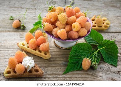 Sweet homemade waffles and fresh yellow raspberries in a bowl on a wooden table.