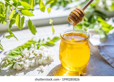 Sweet honey jar surrounded spring acacia blossoms. Honey flows from a spoon in a jar. Sunny light, shallow depth of the field.