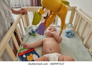 Sweet Infant Child In Crib, Top View. Large Colorful And Noisy Toy Over Baby To Attract Attention. Educational Toys For Young Kids.