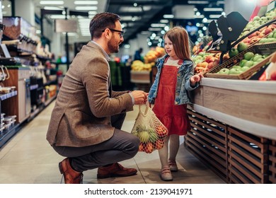 Sweet Kid Helping Her Dad Shop For Fruits At The Supermarket.