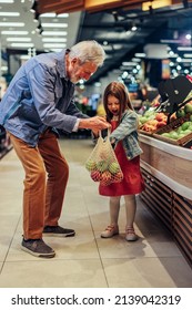 Sweet Kid Helping Her Grandfather Shop For Fruits At The Supermarket