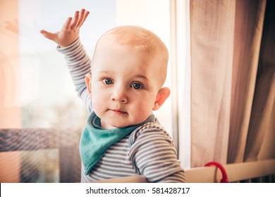 Sweet Little Boy In Baby Blue Striped Cotton Top And Turquoise Teal Bib Waving Hello To His Doggy Friend In The Garden Behind Window And Looking Into Camera