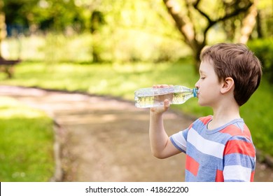 Sweet little boy drinking mineral water from the plastic bottle  in the park - Powered by Shutterstock