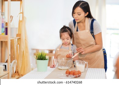 Sweet Little Cute Girl Is Learning From Her Mom How To Make A Cake, In The Home Kitchen.