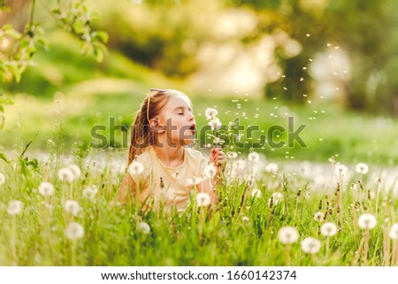 Sweet little girl blowing dandelion sitting between dandelions