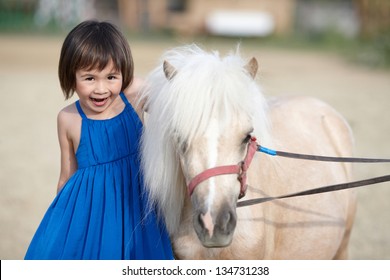 Sweet little girl in blue dress with her white pony